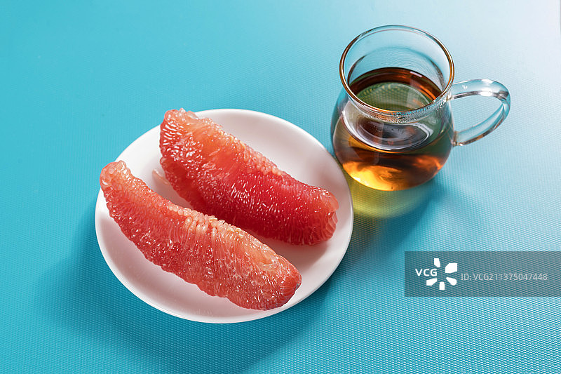 一盘红心柚子和茶水摆放在桌面上图片素材