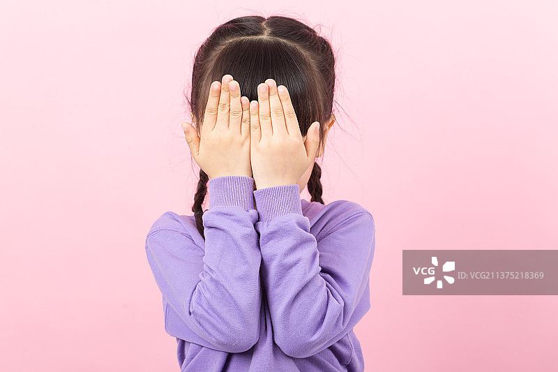 粉色背景前双手捂脸伤心的亚洲小女孩图片素材