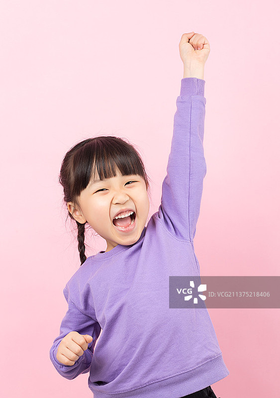 粉色背景前高举手臂的亚洲小女孩图片素材