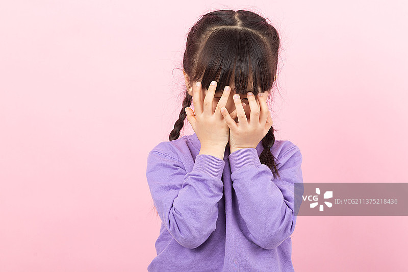 粉色背景前的亚洲小女孩用手捂脸图片素材