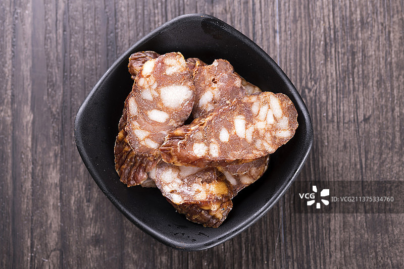 一盘麻辣腊肠摆放在木桌面上特写深色调图片素材