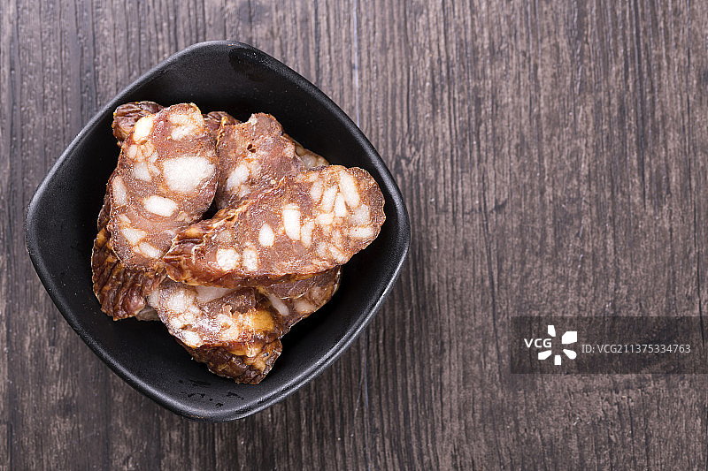 一盘麻辣腊肠摆放在木桌面上特写深色调图片素材