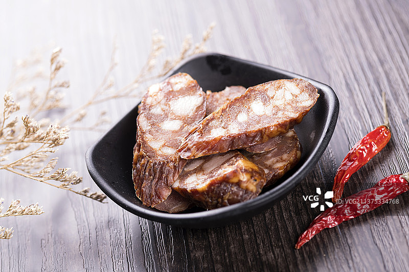 一盘麻辣腊肠摆放在木桌面上特写深色调图片素材