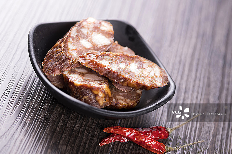 一盘麻辣腊肠摆放在木桌面上特写深色调图片素材