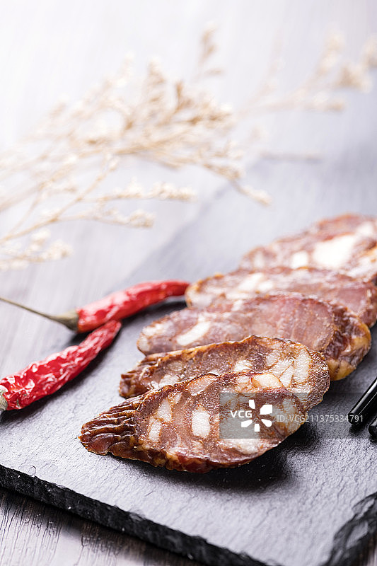 一盘麻辣腊肠摆放在木桌面上特写深色调图片素材