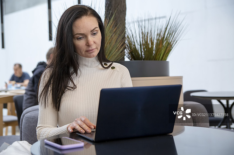 戴口罩的年轻女子在咖啡馆用笔记本电脑工作图片素材