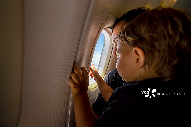 父亲和可爱的幼儿在舷窗欣赏天空，首次飞行概念图片素材