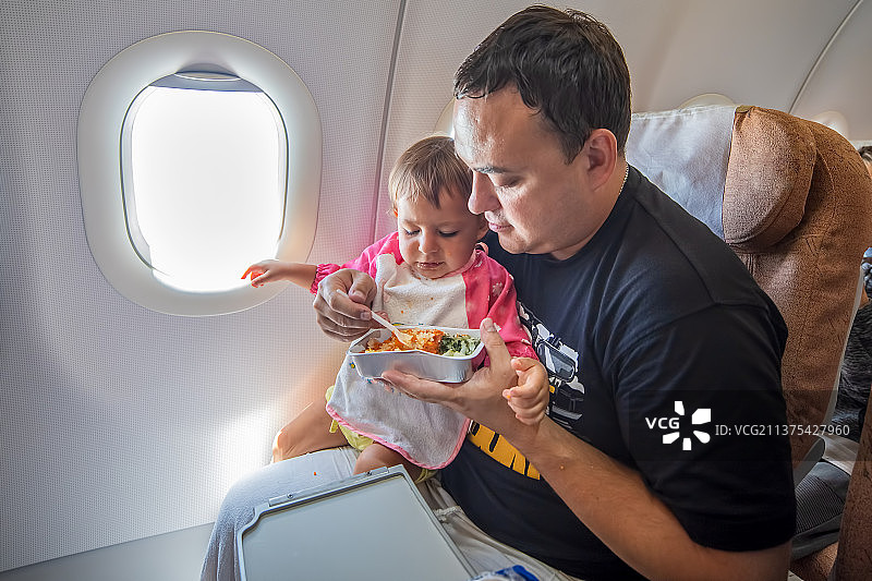 父亲在飞机上给幼儿喂食特制餐点。图片素材