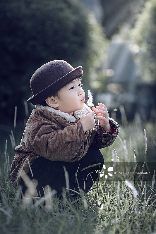 蹲在草丛中吹蒲公英的小男孩图片素材