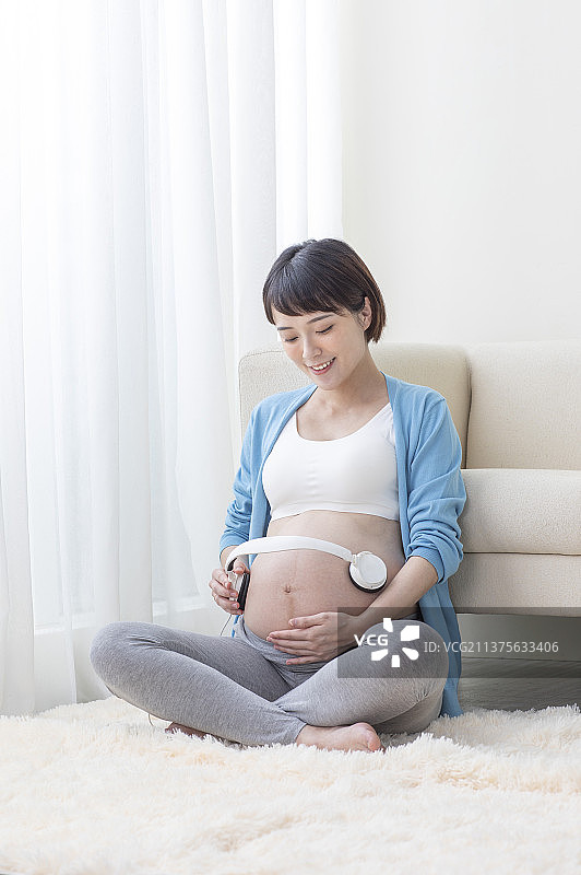 孕妇拿着把耳机放在肚子上进行胎教图片素材