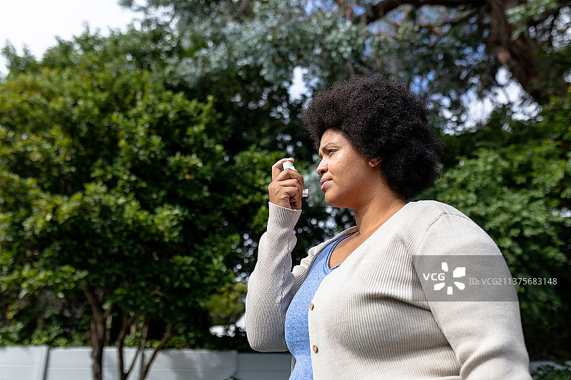 非洲裔中年妇女在树林旁使用哮喘吸入器侧视图图片素材