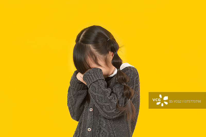 暖黄色背景前的小女孩低头揉着眼睛哭泣图片素材
