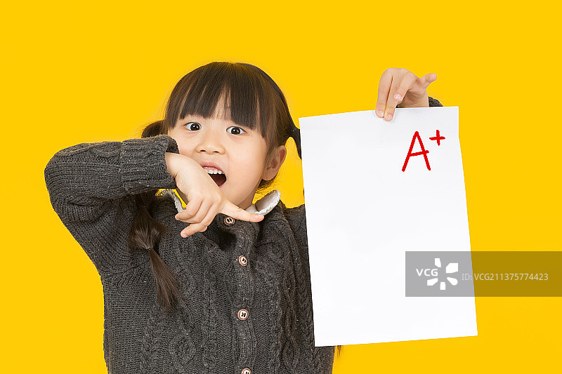 暖黄色背景前拿着试卷的中国小女孩图片素材