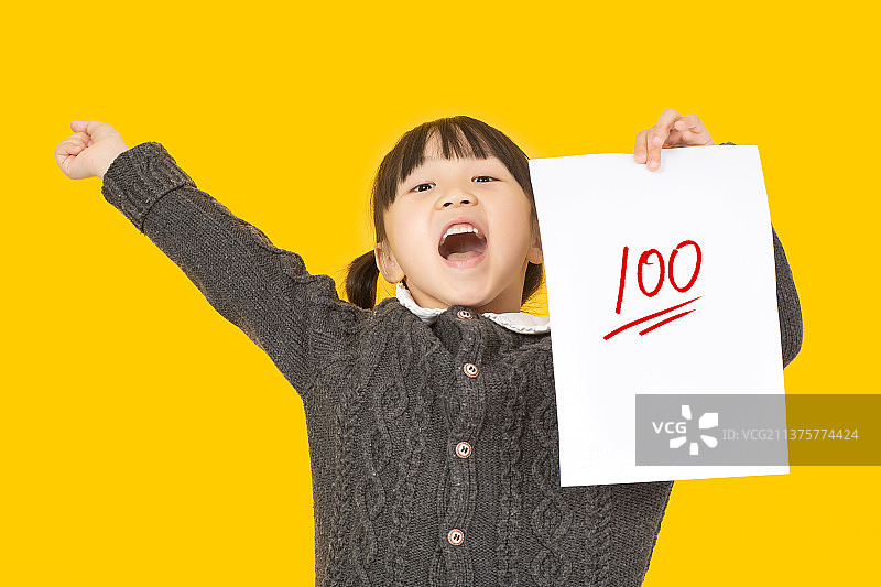 暖黄色背景前拿着试卷的中国小女孩图片素材