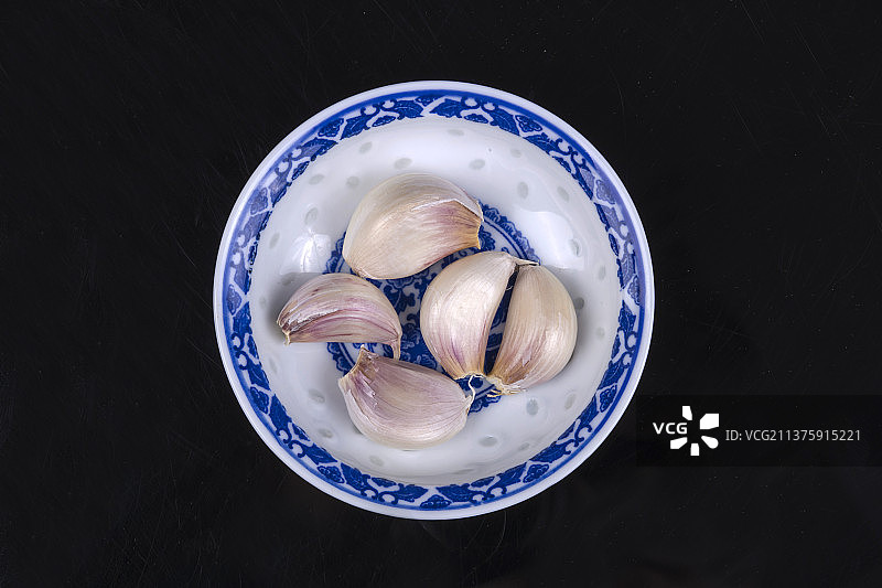 一簸箕大蒜摆放在黑色背景上图片素材