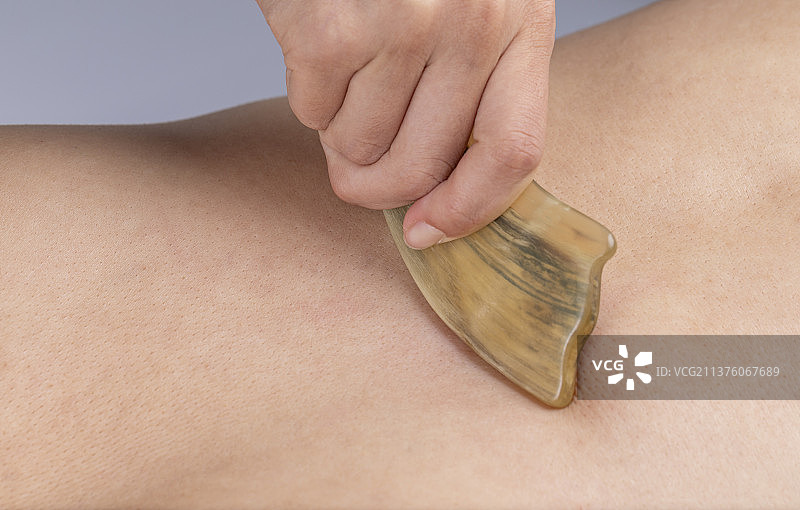 手拿着刮痧板在背部皮肤上采用中医传统疗法为患者刮痧治病图片素材