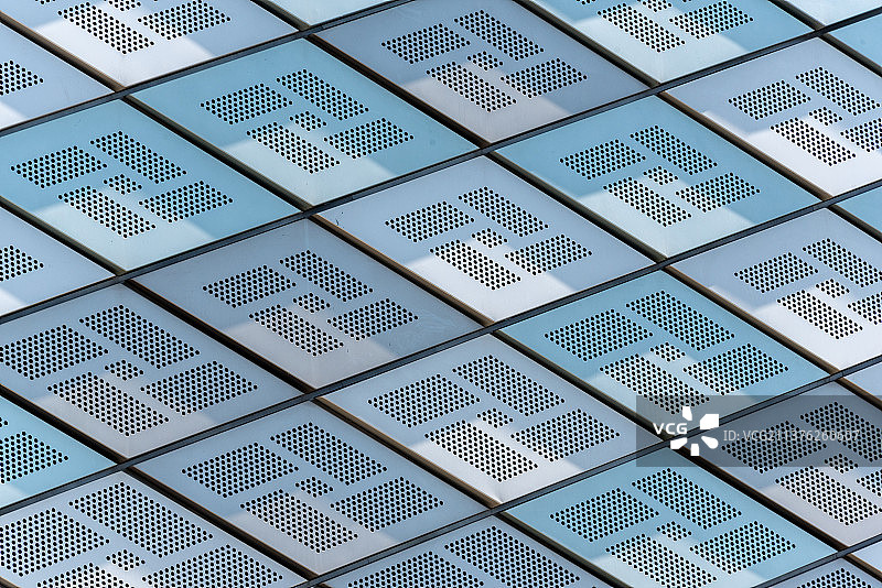 阳光下的金属建筑外墙由一个个规则排列的菱形构成，发射出白色和蓝色的光芒图片素材