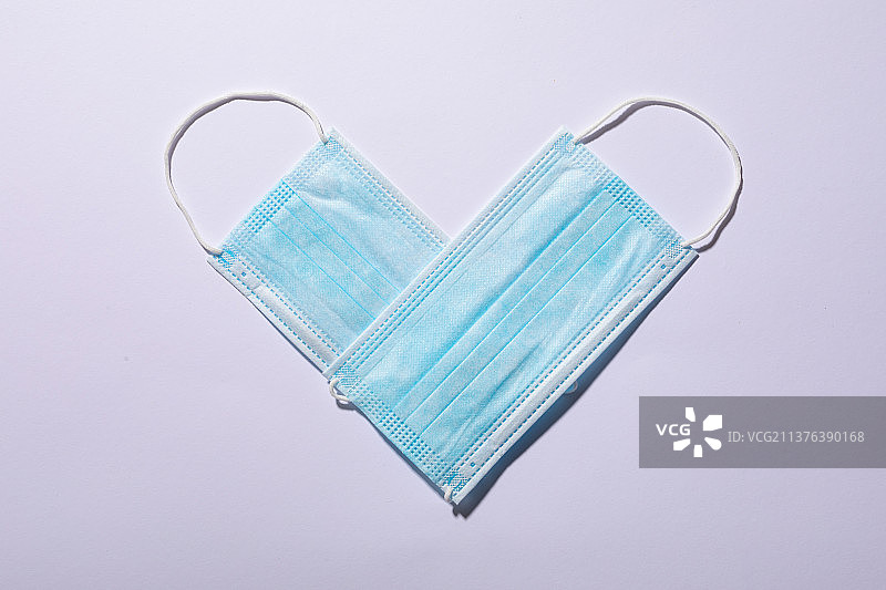 俯视角度拍摄在白色背景上排列成心形的防护口罩，留有复制空间图片素材