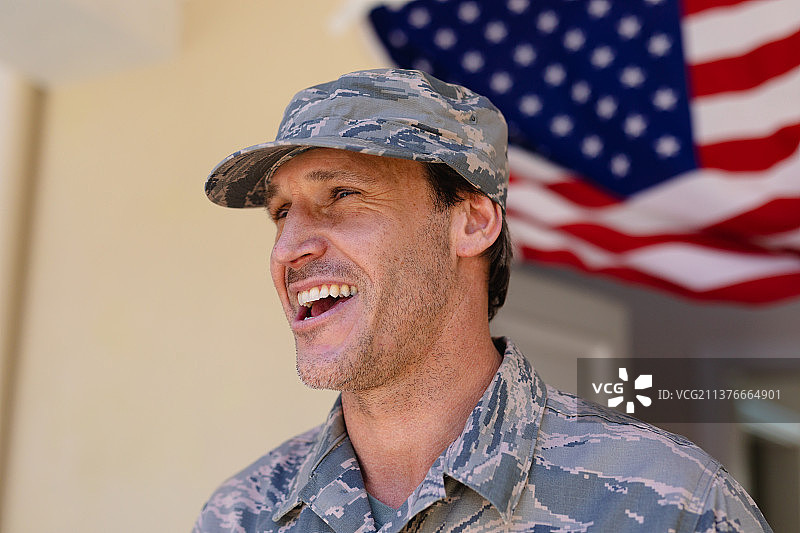 快乐的白人军人戴着帽子，身穿迷彩服，背景是美国国旗图片素材
