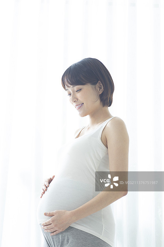 孕妇手摸肚子站着微笑图片素材