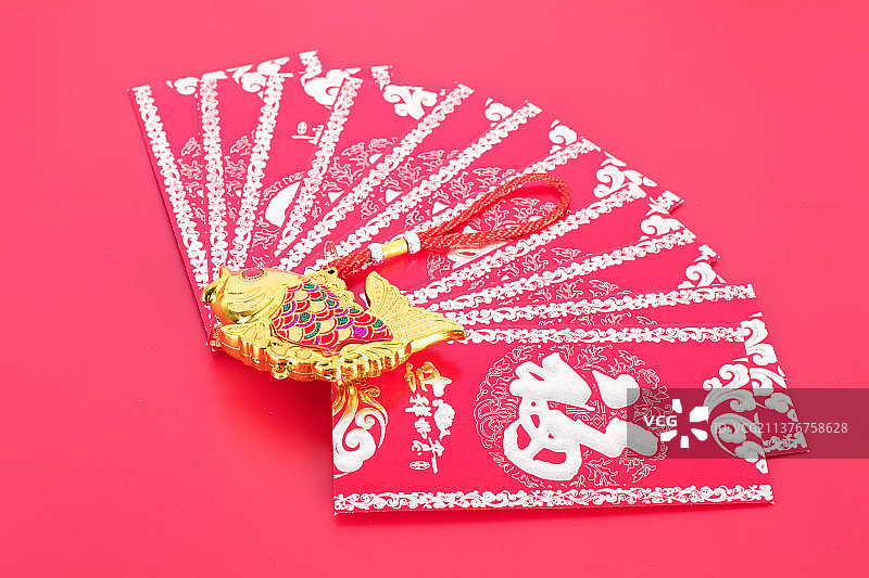 红背景上排开的新年红包和金鱼挂件图片素材