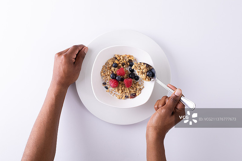 白色背景上用浆果吃格兰诺拉麦片的人手俯视图图片素材