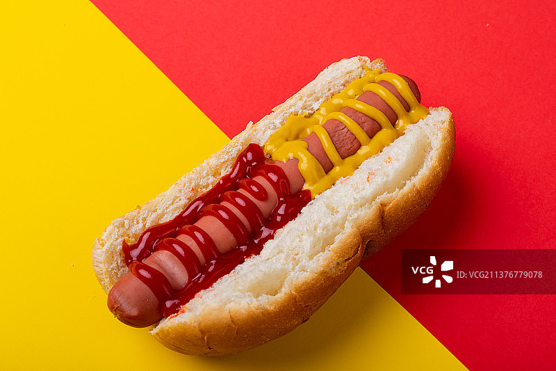 双色背景下涂抹芥末和番茄酱的热狗特写图片素材