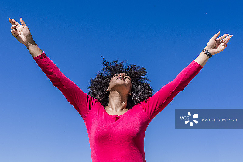 阳光明媚的日子里，非洲裔女子自由地举起双臂图片素材