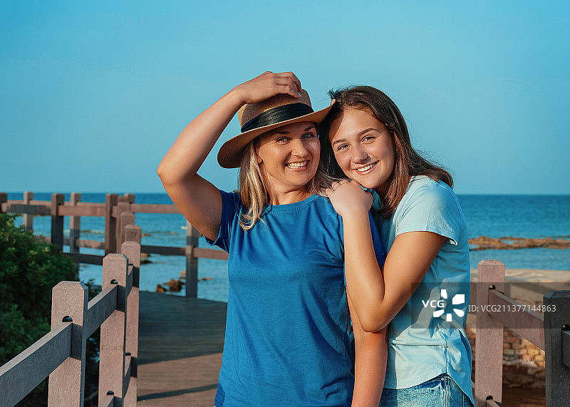 快乐的母亲和十几岁的女儿在码头上拥抱微笑图片素材