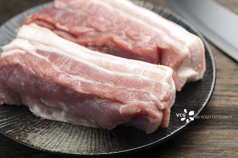 一盘新鲜猪肉与餐刀摆放在木桌面上特写图片素材