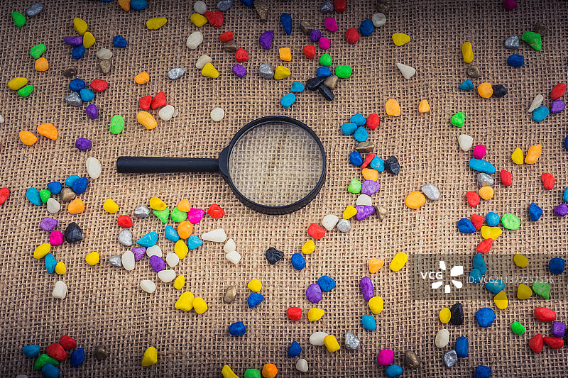 放大镜和鹅卵石，粗麻布上彩色石头的高角度视图图片素材