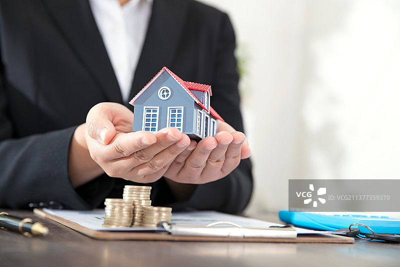 房地产相关从业者手捧小房子模型和相关文件与硬币图片素材