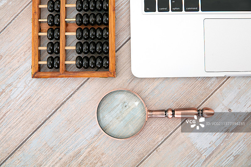 俯视桌子上的笔记本电脑及中国传统计算工具算珠和一个放大镜图片素材