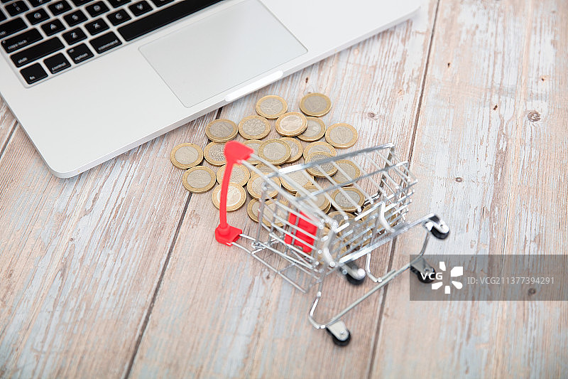 桌子上倾倒的小购物车和散落正在被笔记本电脑吸走的欧元硬币图片素材