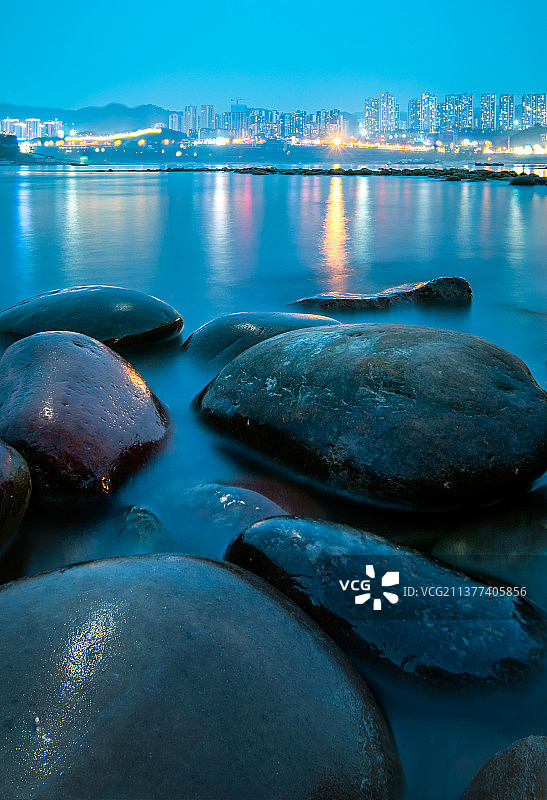 重庆市巴南区，傍晚时分，长江对岸的城市灯火辉煌，前景是圆的石头图片素材
