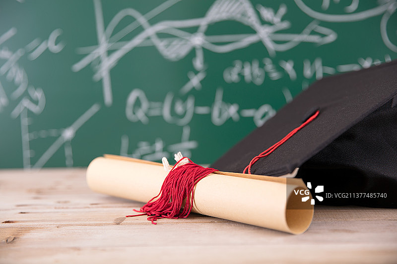黑板前一个博士帽和卷着的毕业证书图片素材