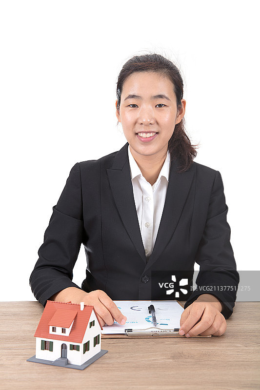 房地产销售人员坐在放着小房子模型的桌子前看着镜头微笑图片素材