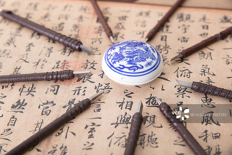 俯视拍摄中国书法作品上被众多钢制刻刀围绕的一盒印泥图片素材