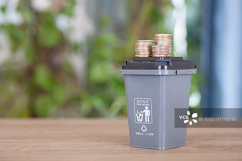 灰色盛放其它垃圾的垃圾桶模型及其盖子上放着一堆美元硬币图片素材