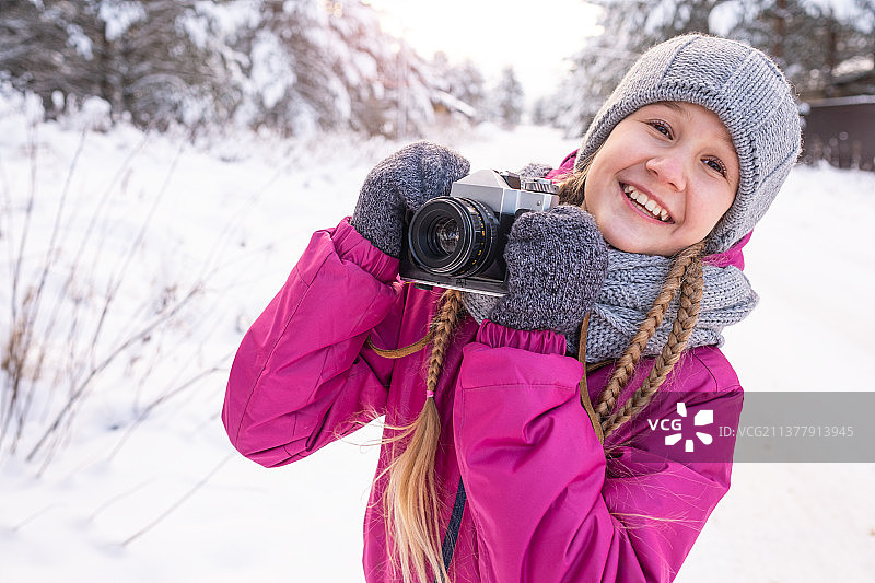 笑容灿烂的女孩站在雪地里手持相机图片素材