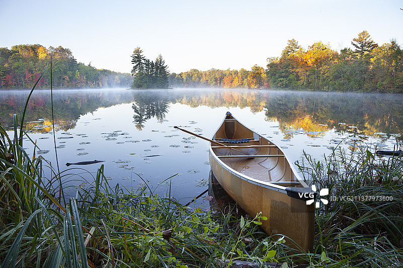 秋季日出时分，平静的湖岸上，岛屿旁的独木舟图片素材
