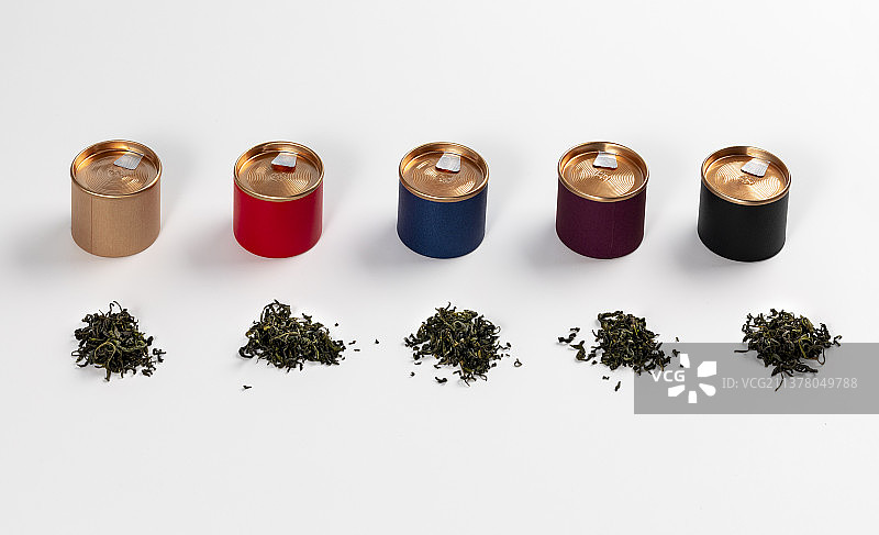 白色背景中整体排列摆放的小罐茶茶桶和零散的茶叶图片素材