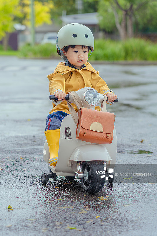 下雨天穿黄色雨衣小男孩在开摩托车游玩图片素材