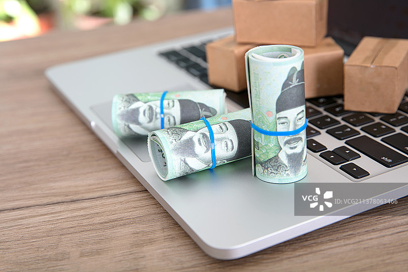 笔记本电脑键盘上卷筒状的韩国纸币和几个快递包裹模型图片素材