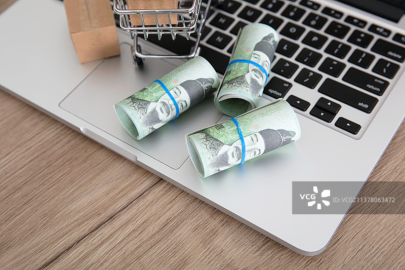 笔记本电脑键盘上一辆满载快递箱的购物车和三卷韩币钞票图片素材