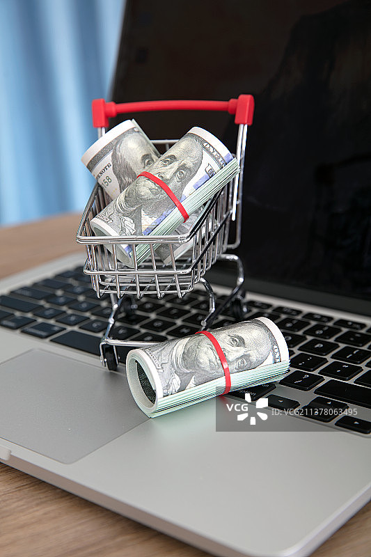 笔记本电脑键盘上装着美元钞票的购物车模型图片素材