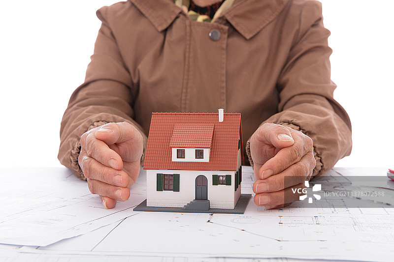 老人双手呵护着图纸上的房子模型图片素材