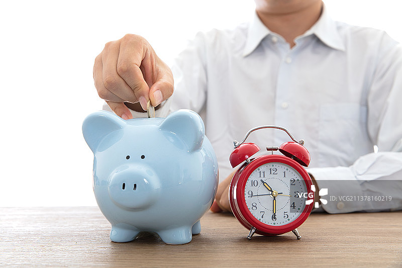 往小猪存钱罐里投硬币和存钱罐旁边一个闹钟图片素材