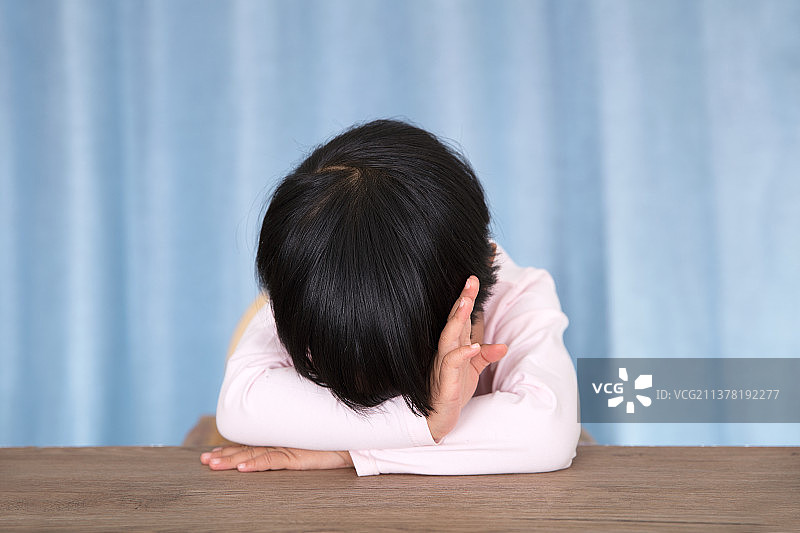 蓝色窗帘背景前趴在桌子上用装睡拒绝的小女孩图片素材