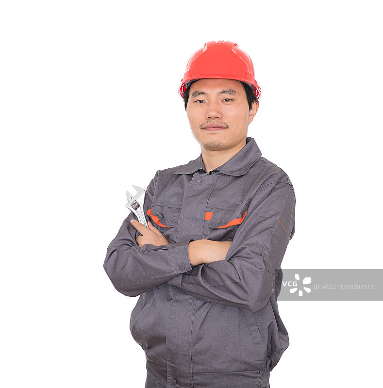 头戴红色安全帽手拿活口扳子的工人抱着胳膊站在白背景前图片素材
